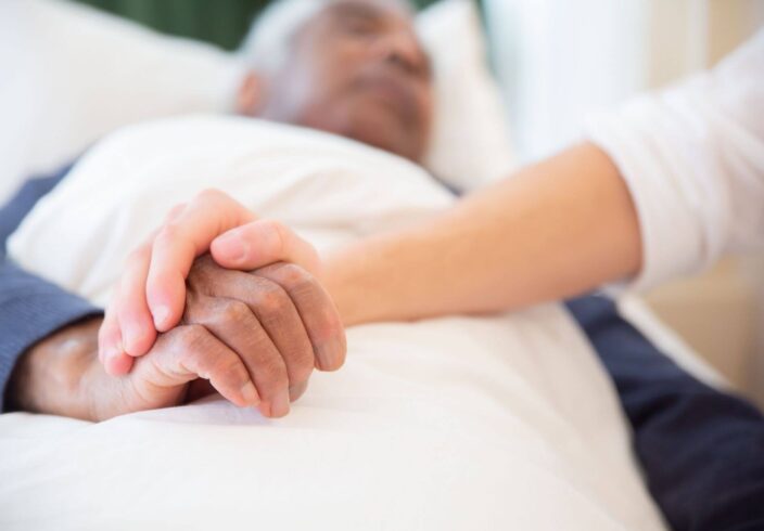 Holding hands with an elderly man in bed